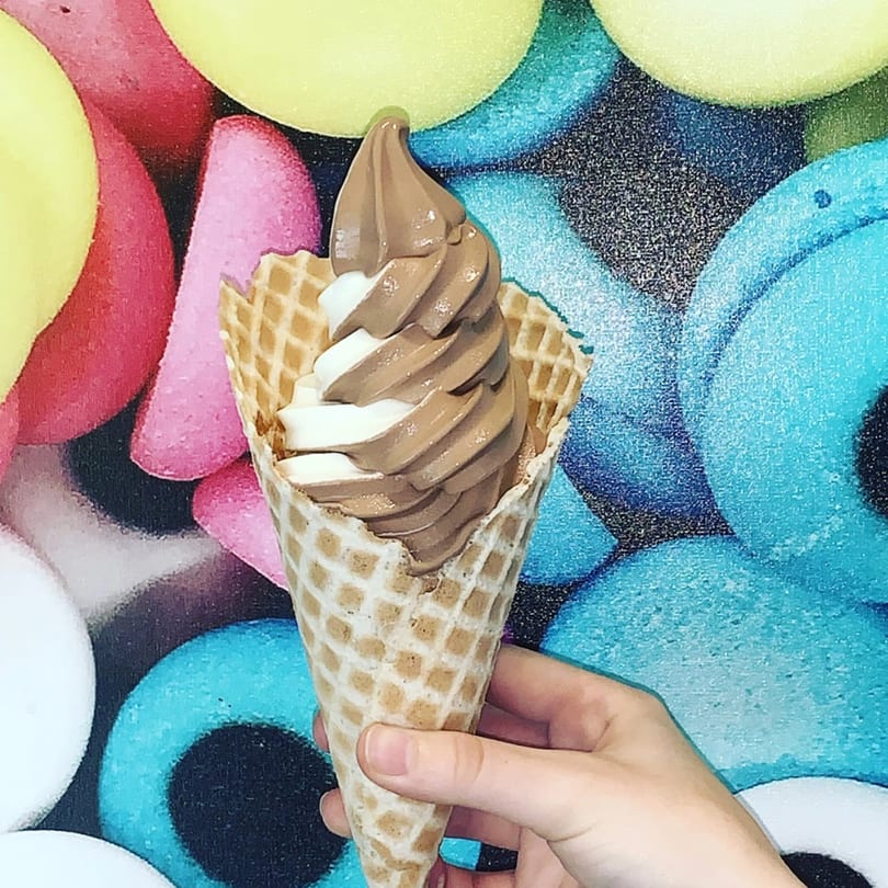 A hand holds a waffle cone with swirled chocolate and vanilla soft-serve ice cream.