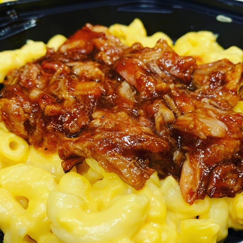 Close-up of macaroni and cheese topped with generous portions of barbecue pulled pork.